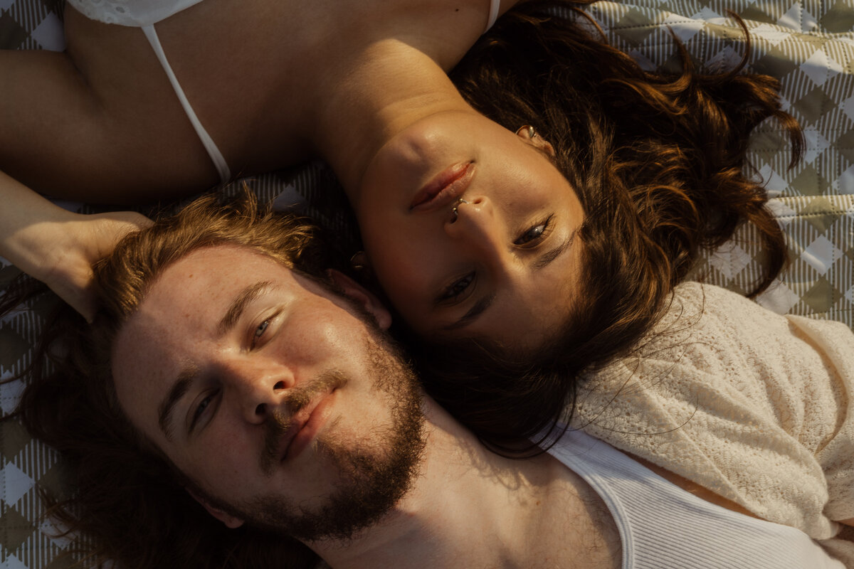 A relaxed and loving shot of the couple lying side by side on the grass, surrounded by nature at White Rock Lake park.