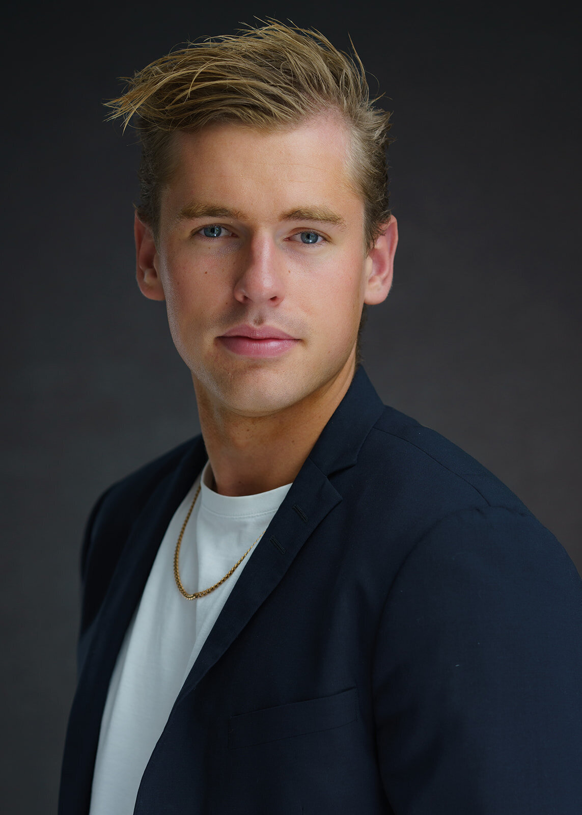 Young man with blonde hair in a blue jacket and a white teeshirt posing for a portrait during a modeling portfolio photo session