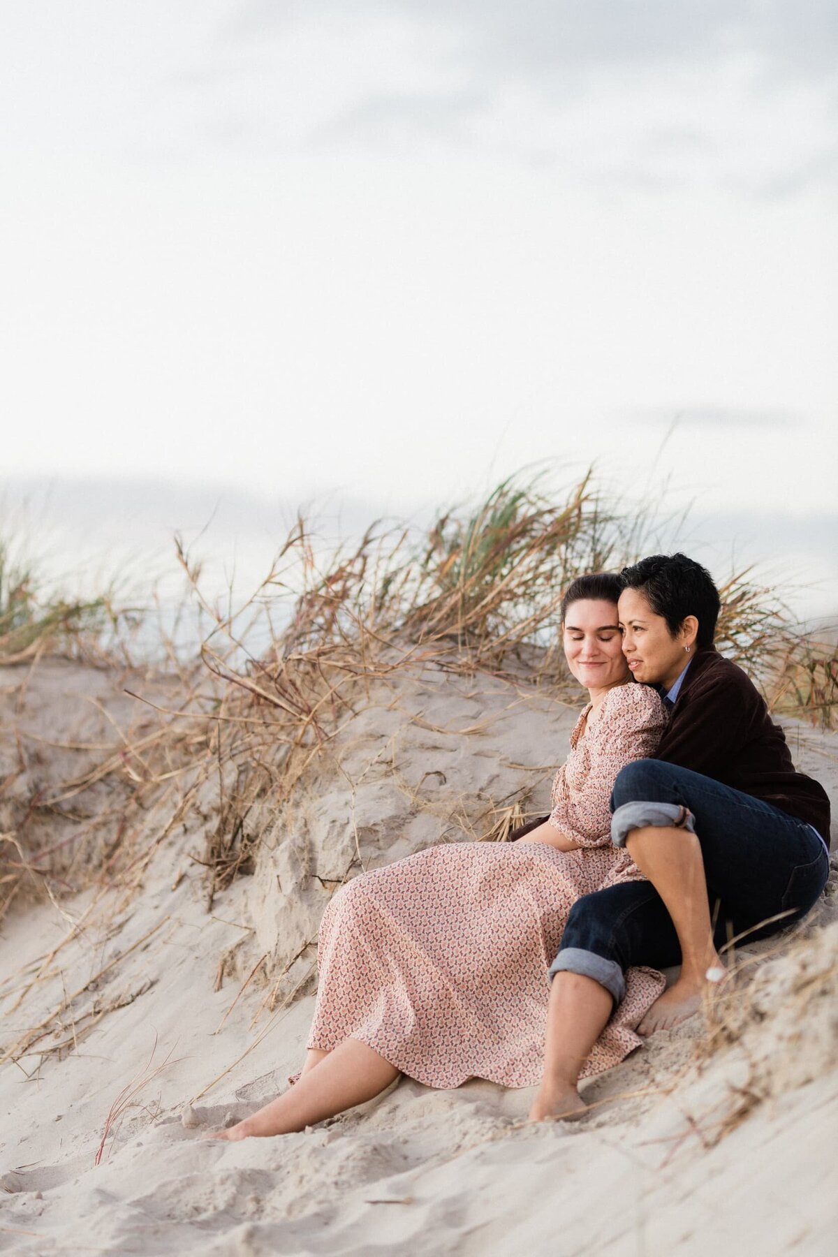 Two brides to be sitting on a sand dune
