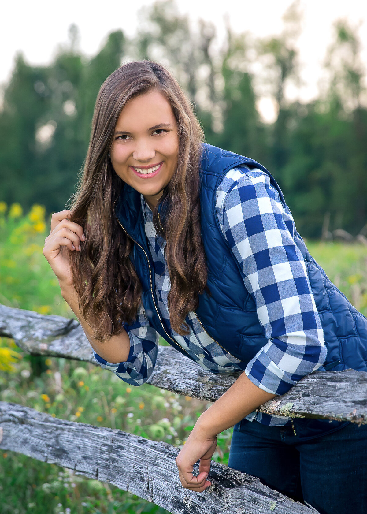 Fall senior portrait taken by a fence at a farm
