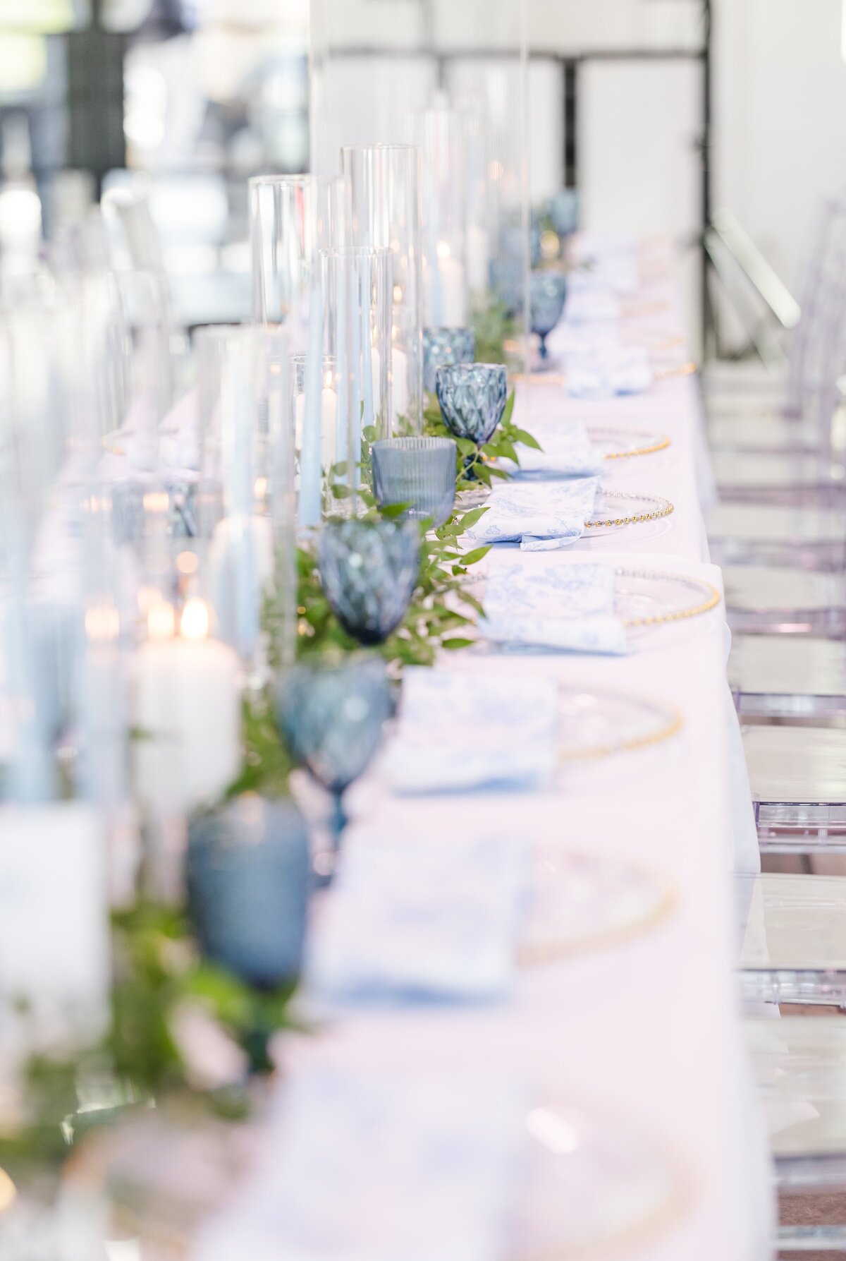 Details of a long family style reception table with blue glass and candles