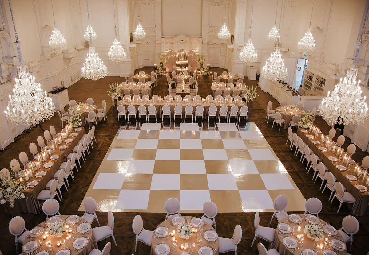 Elegant table settings and crystal chandeliers surround a checkerboard dancefloor for a wedding at Maison Principale.