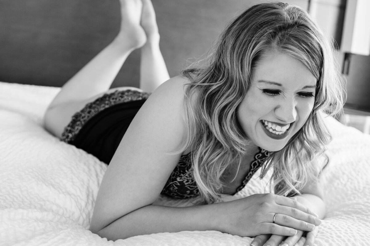 Black and white boudoir photo woman laughing in bed