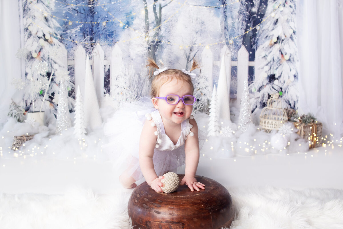 Baby girl wearing purple glasses sitting on wood bowl during cake smash photoshoot with Franklin Tennessee cake smash photographer
