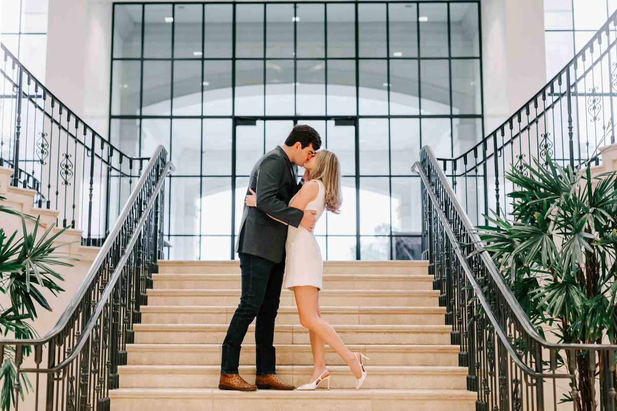 natalie and michael stand on the staircase at Lakeway Country Club in Houston, and kiss during their engagement photos.