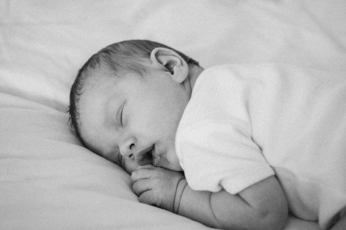 Newborn baby sleeping on a bed, facing slightly to the side with one hand under their cheek.