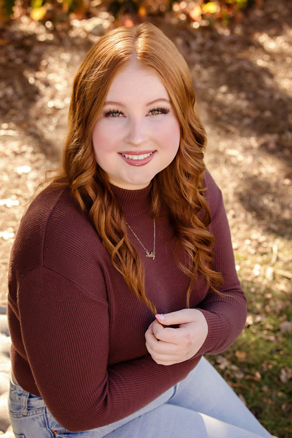 High school senior in cranberry shirt and jeans sitting in South Charlotte park with golden tones and a warm breeze on an Autumn day