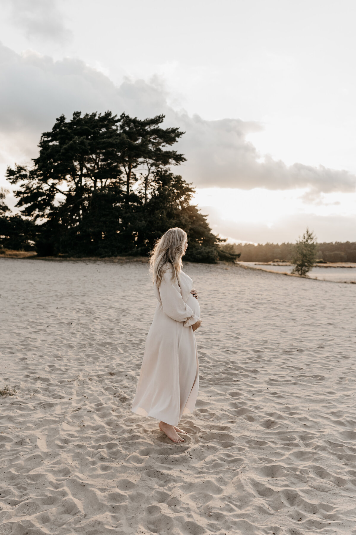 Zwangere vrouw kijkt naar zonsondergang tijdens zwangerschapsshoot.
