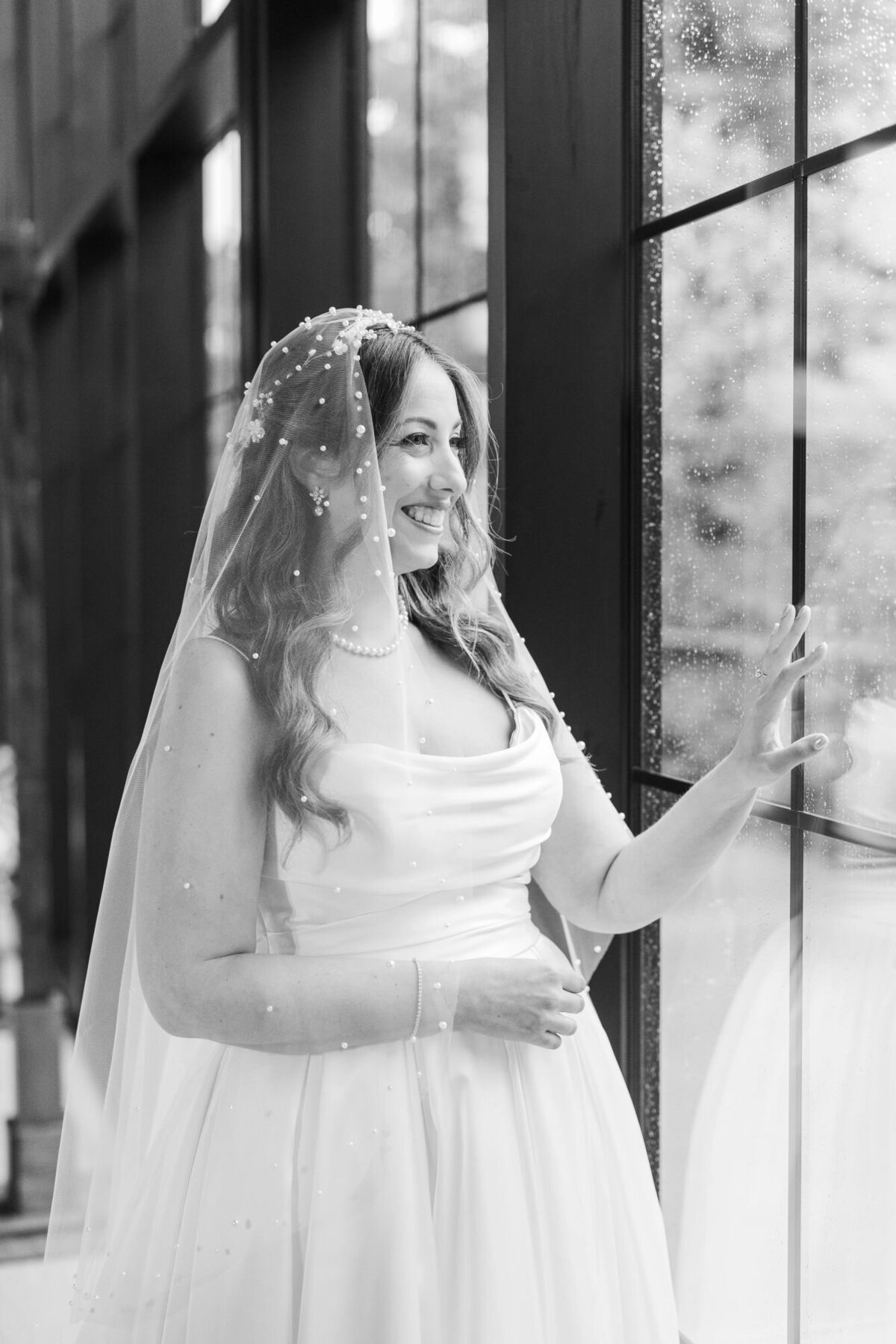 Bride with veil looks out the window in the Roundhouse Hotel wedding ceremony space during a rainstorm