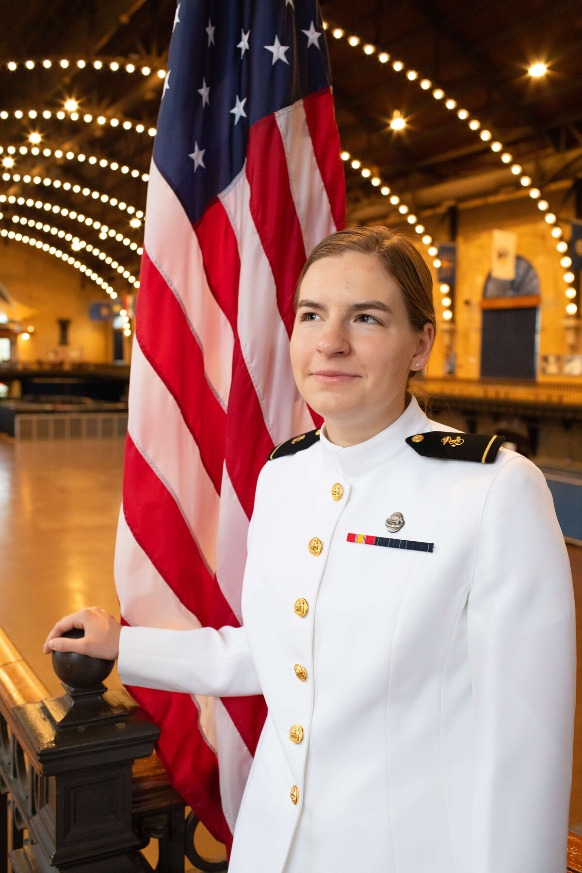 Woman Naval Academy graduate in white uniform with a flag.