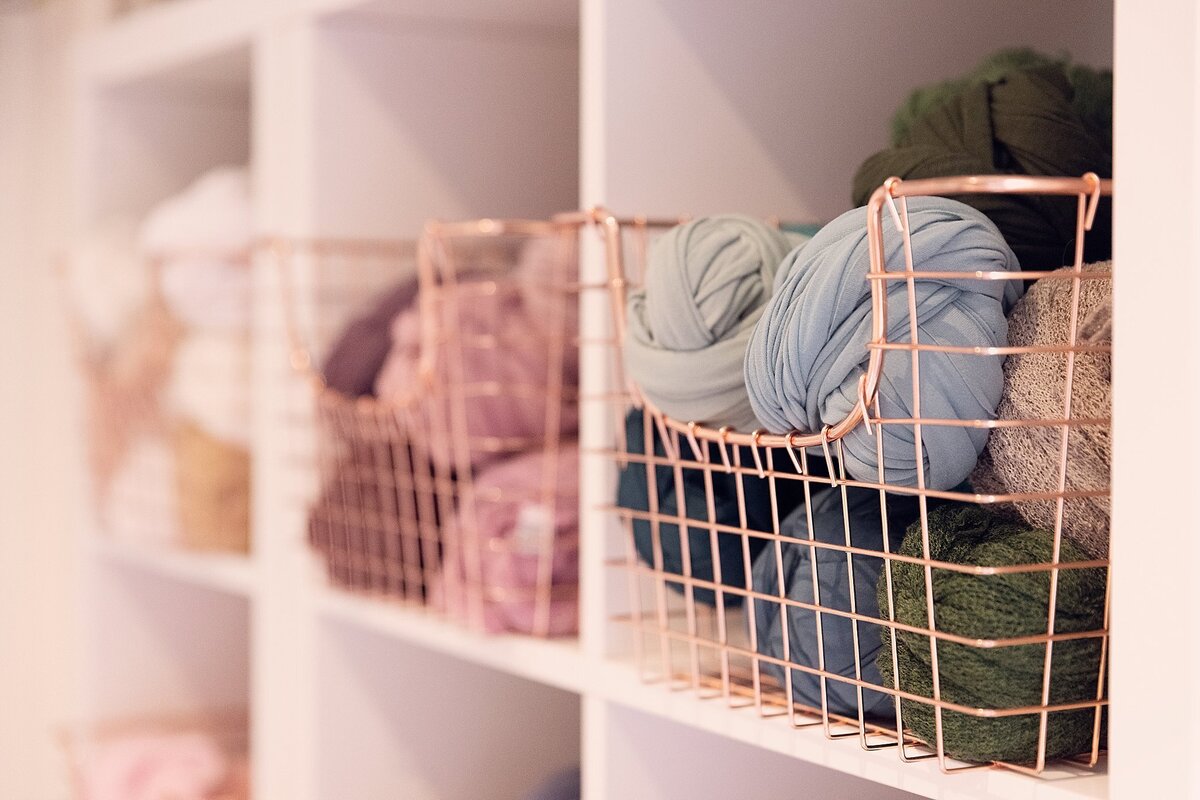 Organized shelving corner in a newborn photography studio displaying baskets of wraps, fabrics, and neatly stored props.
