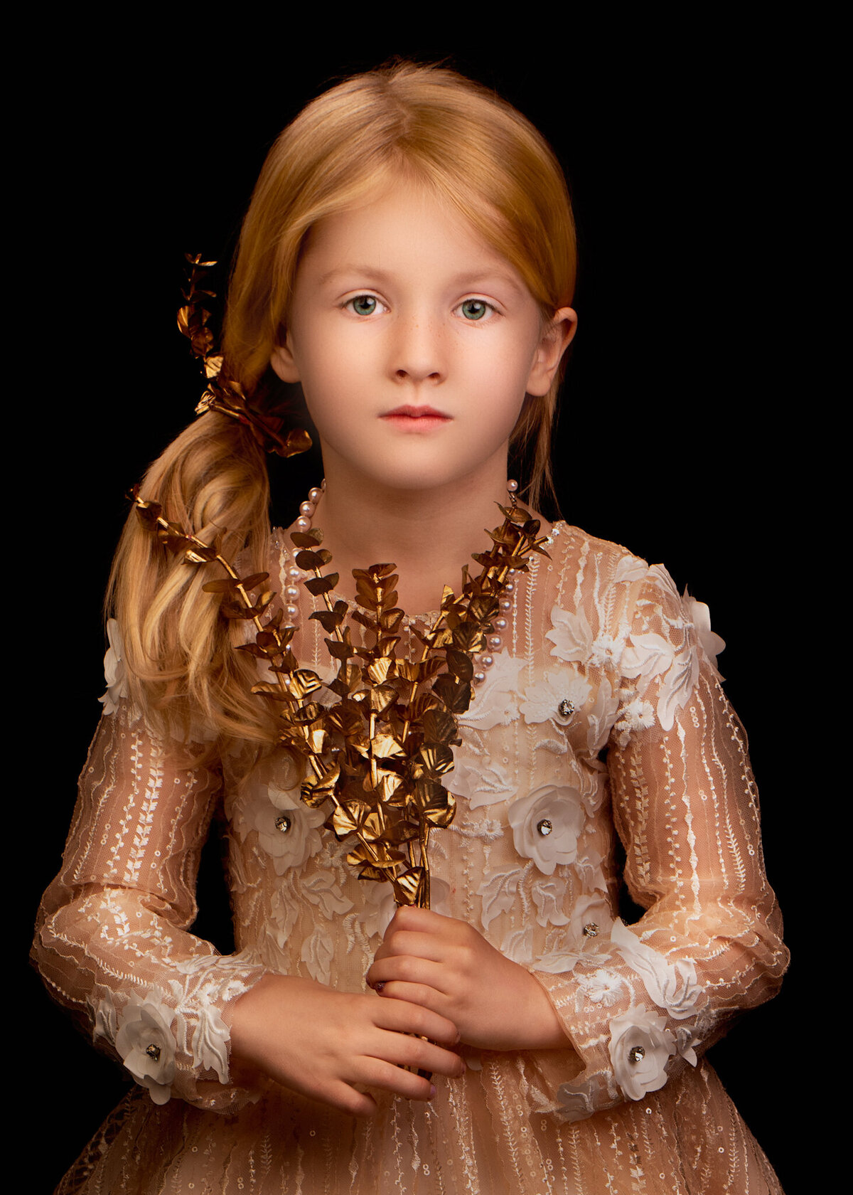 Sophisticated fine art portrait of a young girl wearing a delicate lace dress adorned with golden floral accents, set against a dramatic dark backdrop. Captured in Overland Park, Kansas, this refined setup is perfect for families seeking timeless and artistic child photography.
