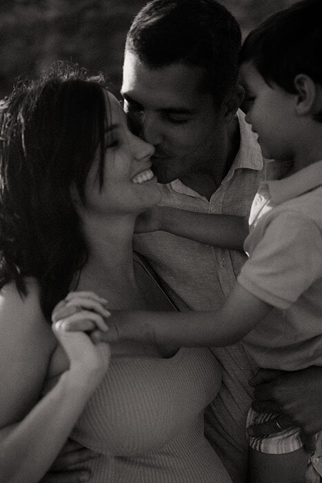 Papa tenant son petit garçon dans les bras et embrassant la maman. Photographie en noir et blanc par Kamescop, photographe en bretagne.