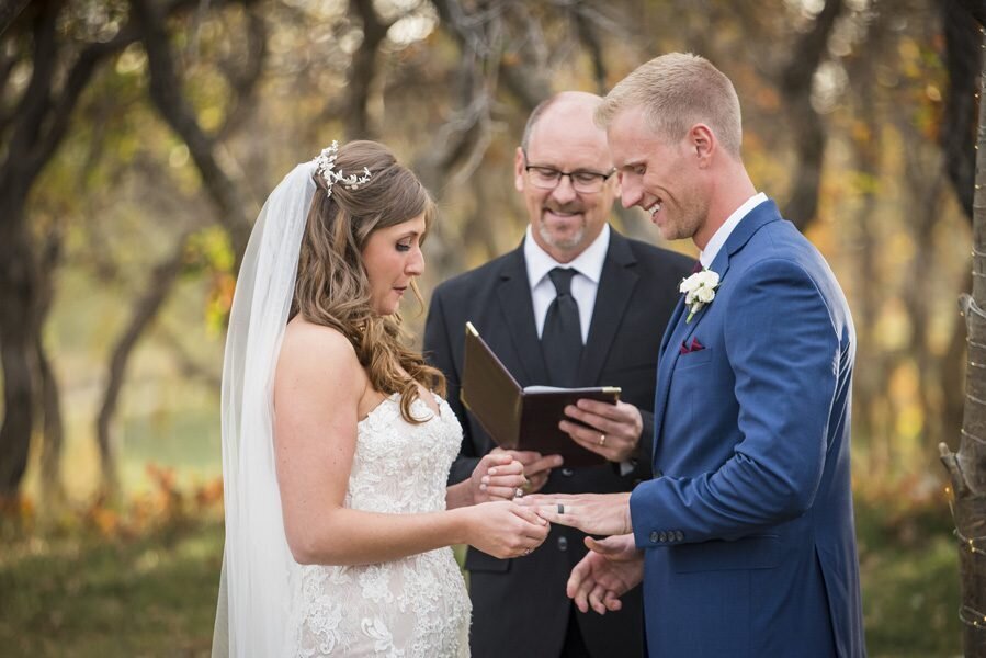 A bride places the wedding band on her groom's finger during the ceremony at The Oaks at Plum Creek.