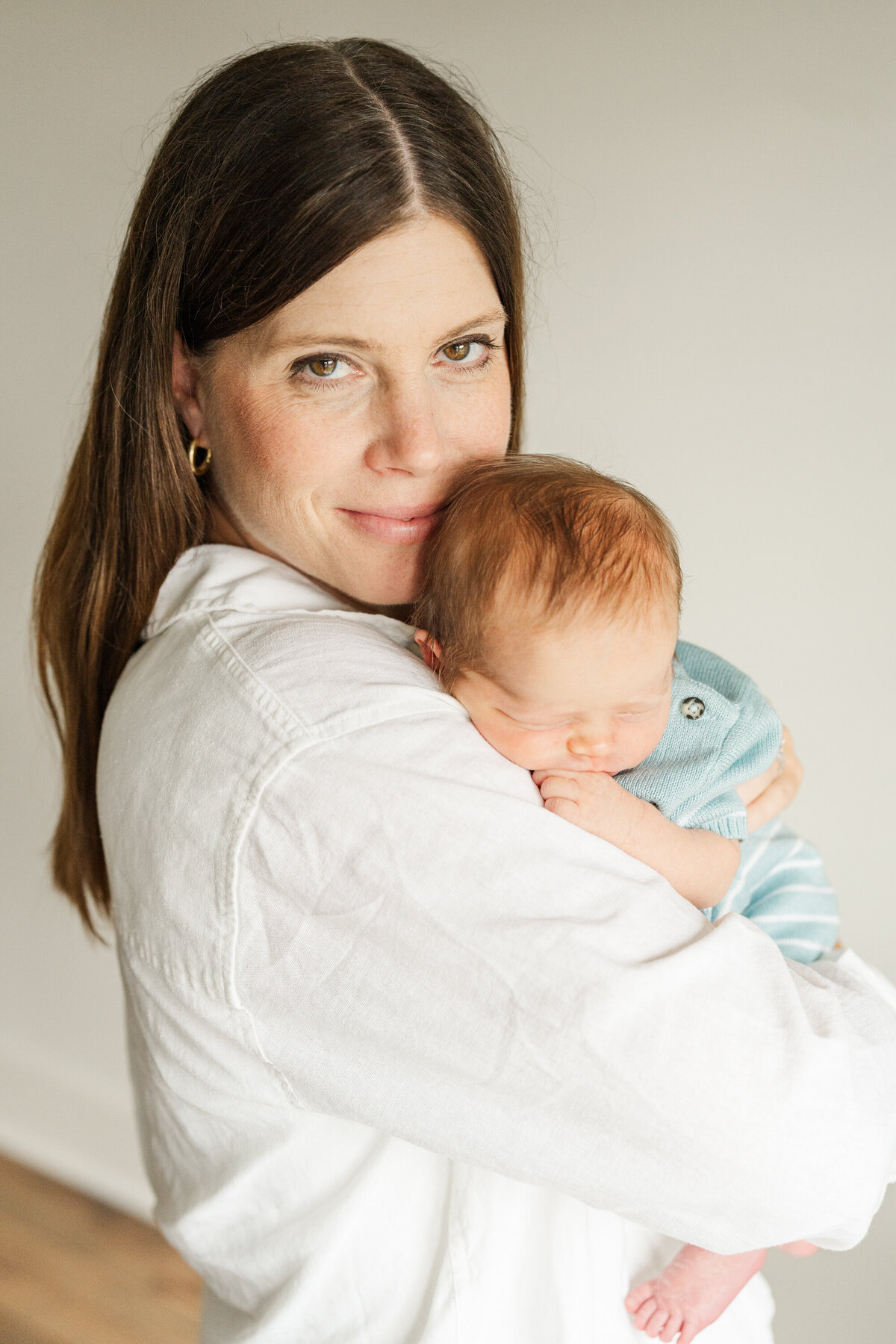 A mother smiles at the camera while gently holding her sleeping newborn close to her chest