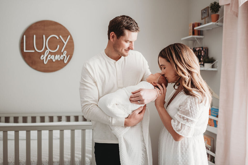 mom kissing newborn baby while dad holds her in nursery for denver photographer
