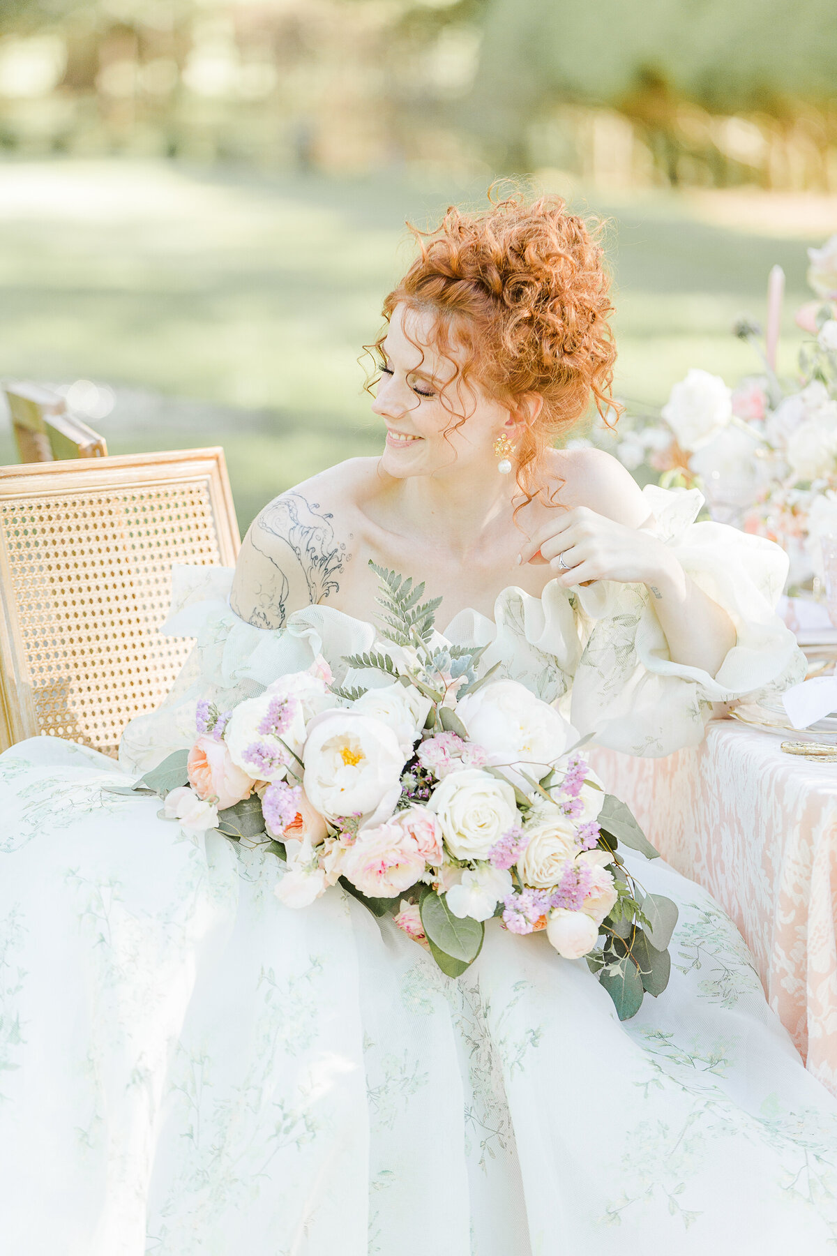A bride is laughing over her shoulder at her wedding reception in the French Countryside. She is holding her large floral bouquet. Captured by New England Destination and Elopement Wedding Photographer Lia Rose Weddings