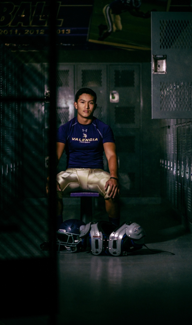 high school senior boy in football locker room in football uniform