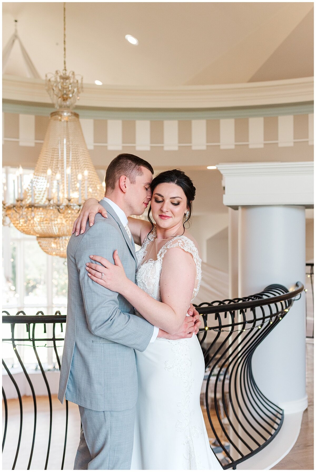 Bride and groom embrace in the loft as groom nuzzles her temple and bride looks down her arm with her eyes closed standing in front of a black banister