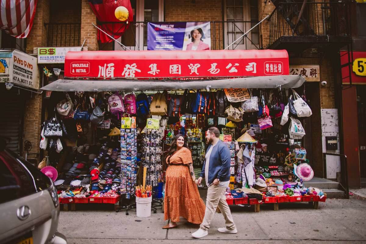 An engaged couple walking near a small shop in chinatown nyc during their engagement session
