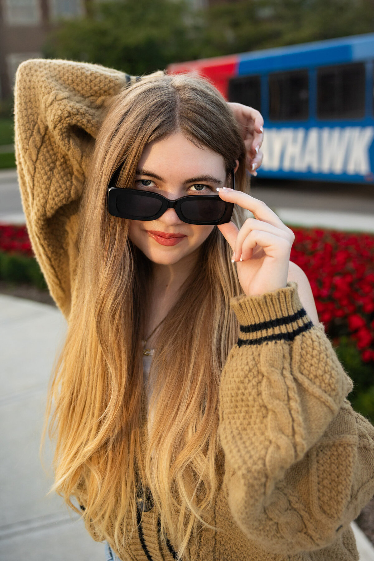A senior girl looking over her sunglasses with her right hand behind her head on the KU campus in Lawrence, KS