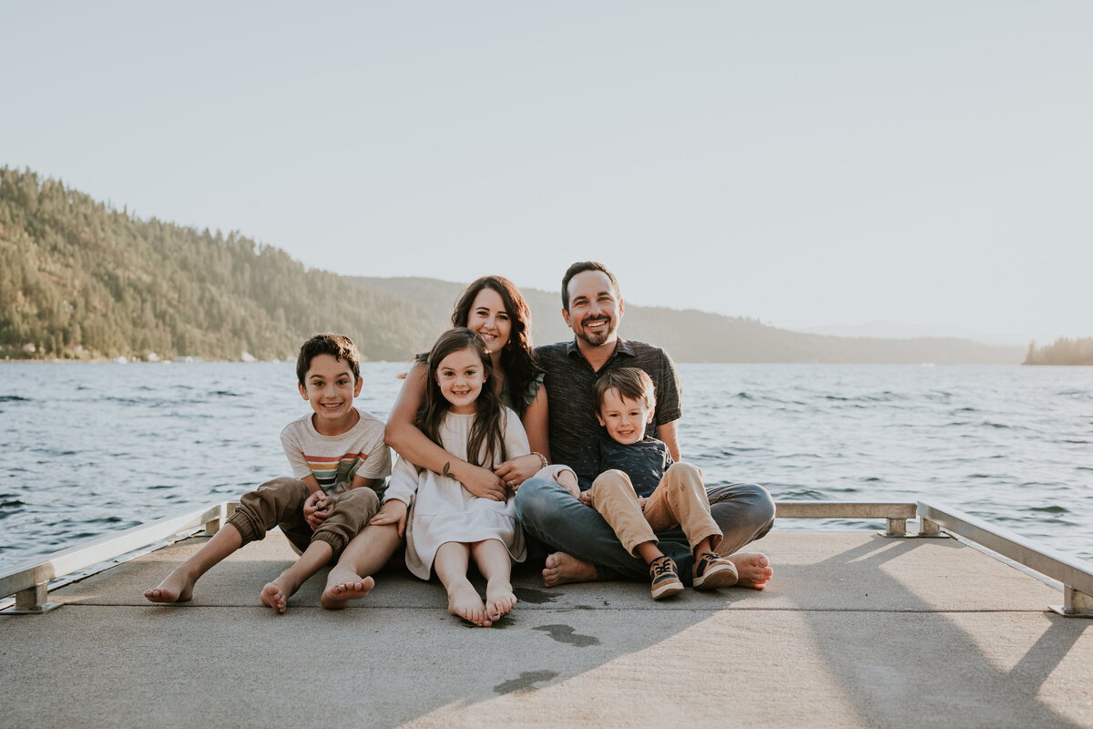 Family of five sits on dock together while smiling at camera.