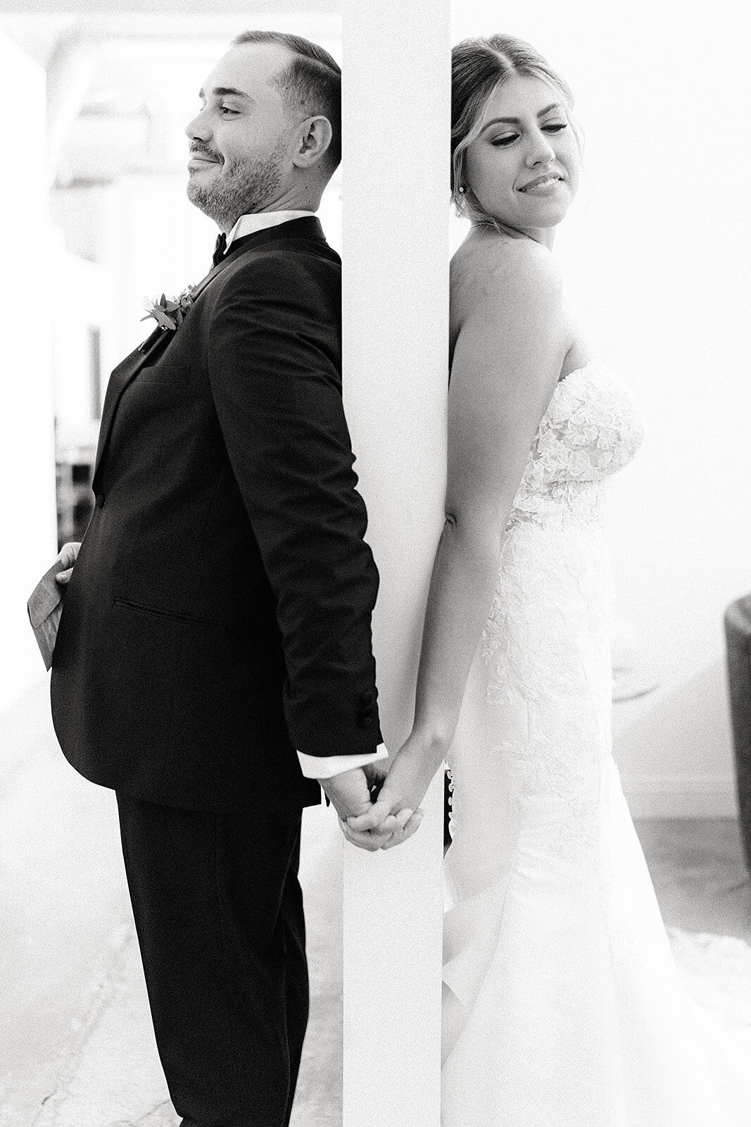 Black and white portrait of the bride and groom holding hands, each facing away but connected, capturing an intimate pre-ceremony moment.