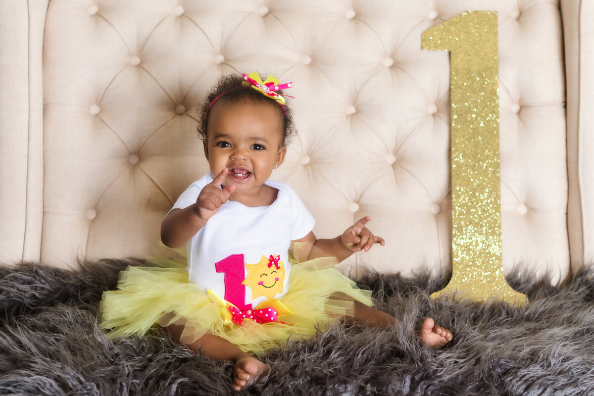 Cake Smash Photographer, a baby sits on a shag rug with a large glittery number one beside her