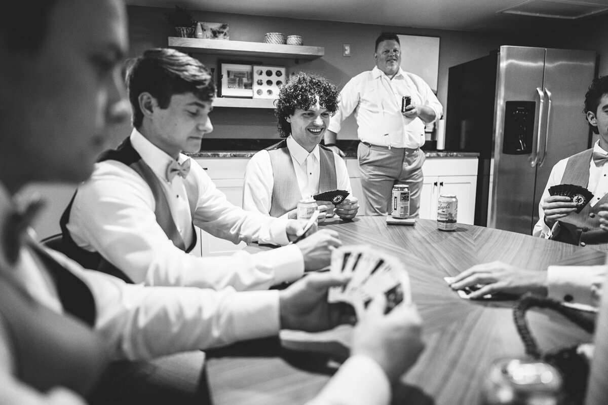 a black and white image of a groom and his groomsmen dressed for a wedding and playing cards in the Willowbrook wedding venue preparation cottage getting ready suite