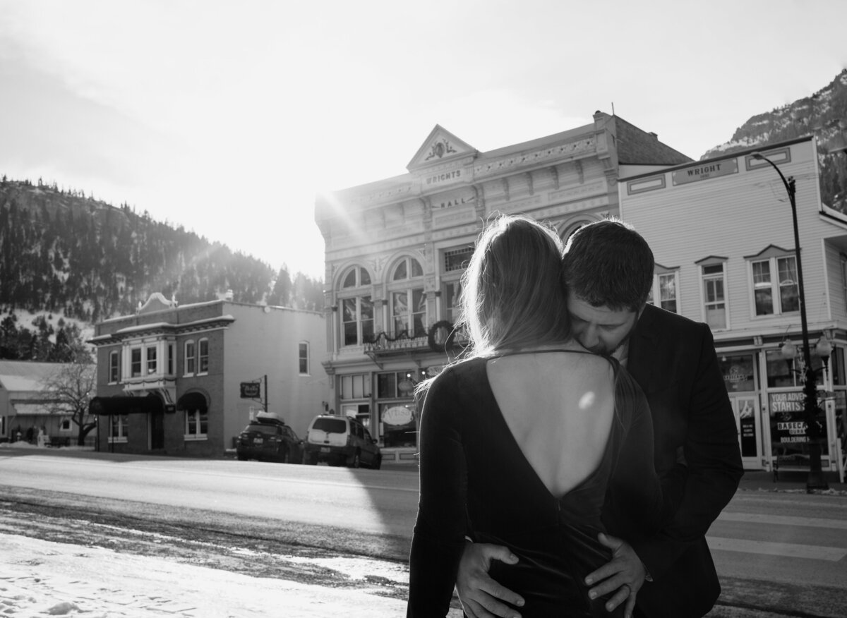 Groom kisses the brides shoulder as they stand in the street of the charming town of Ouray, Colorado after their elopement