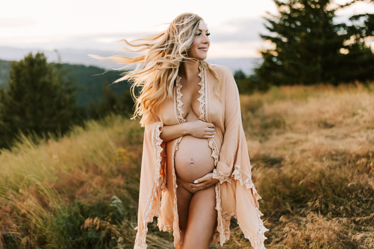 Pregnant woman holding bare belly wearing a robe in a field by Ottawa Portrait Photographer