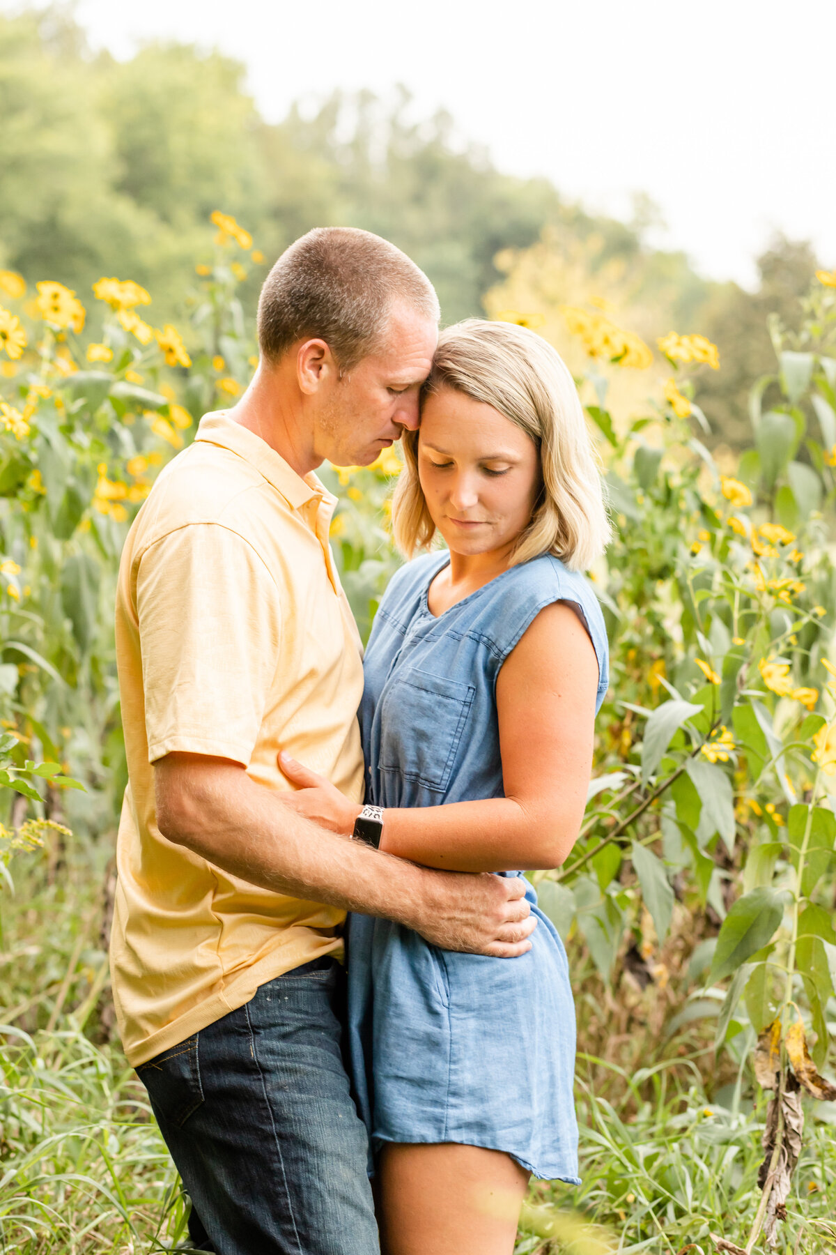 Couple in tall flowers while woman softly looks down and man leans into woman with his nose touching her temple