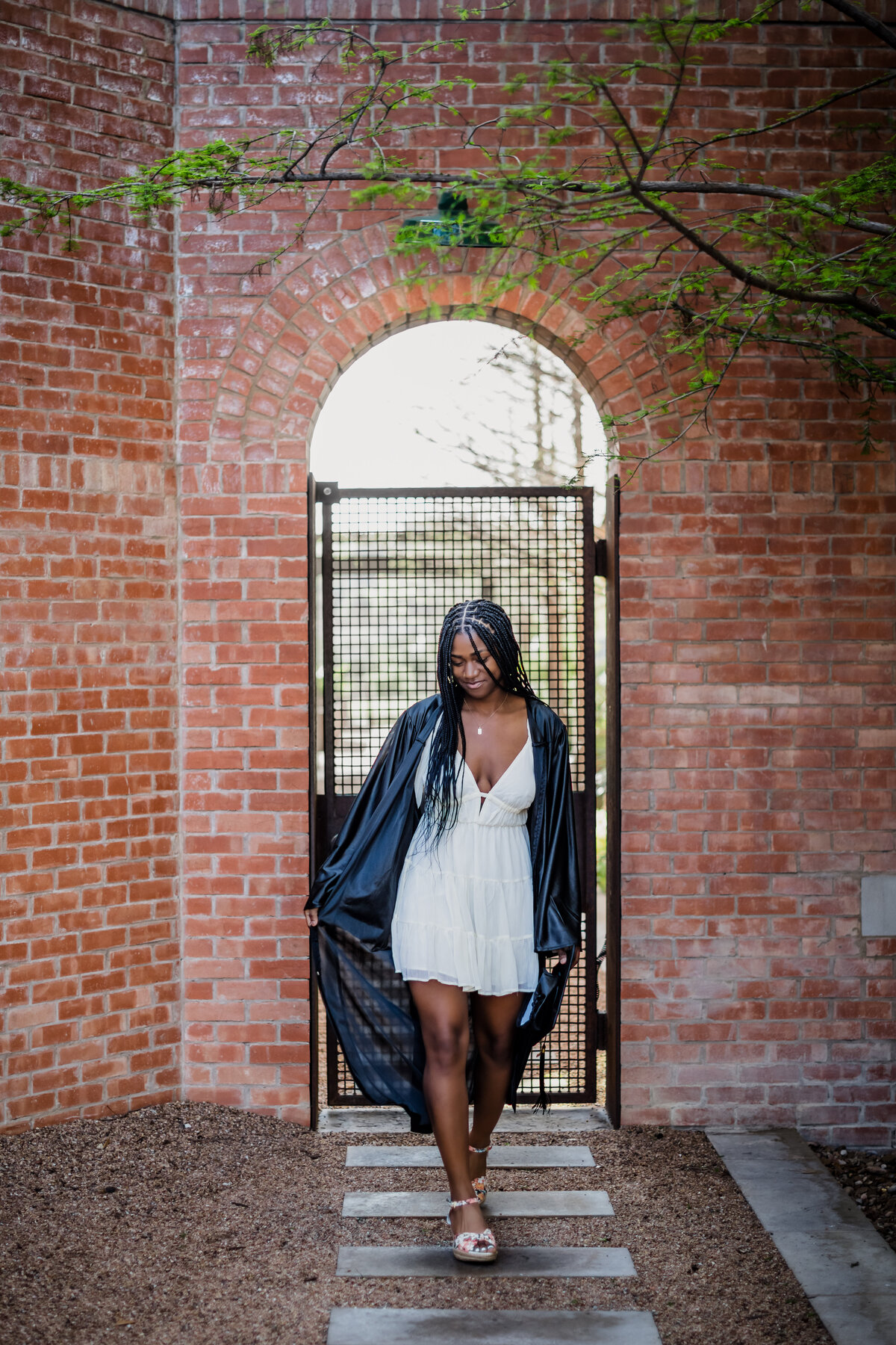 Steel High School senior girl walking through The Pearl in San Antonio wearing a white dress and black graduation gown.