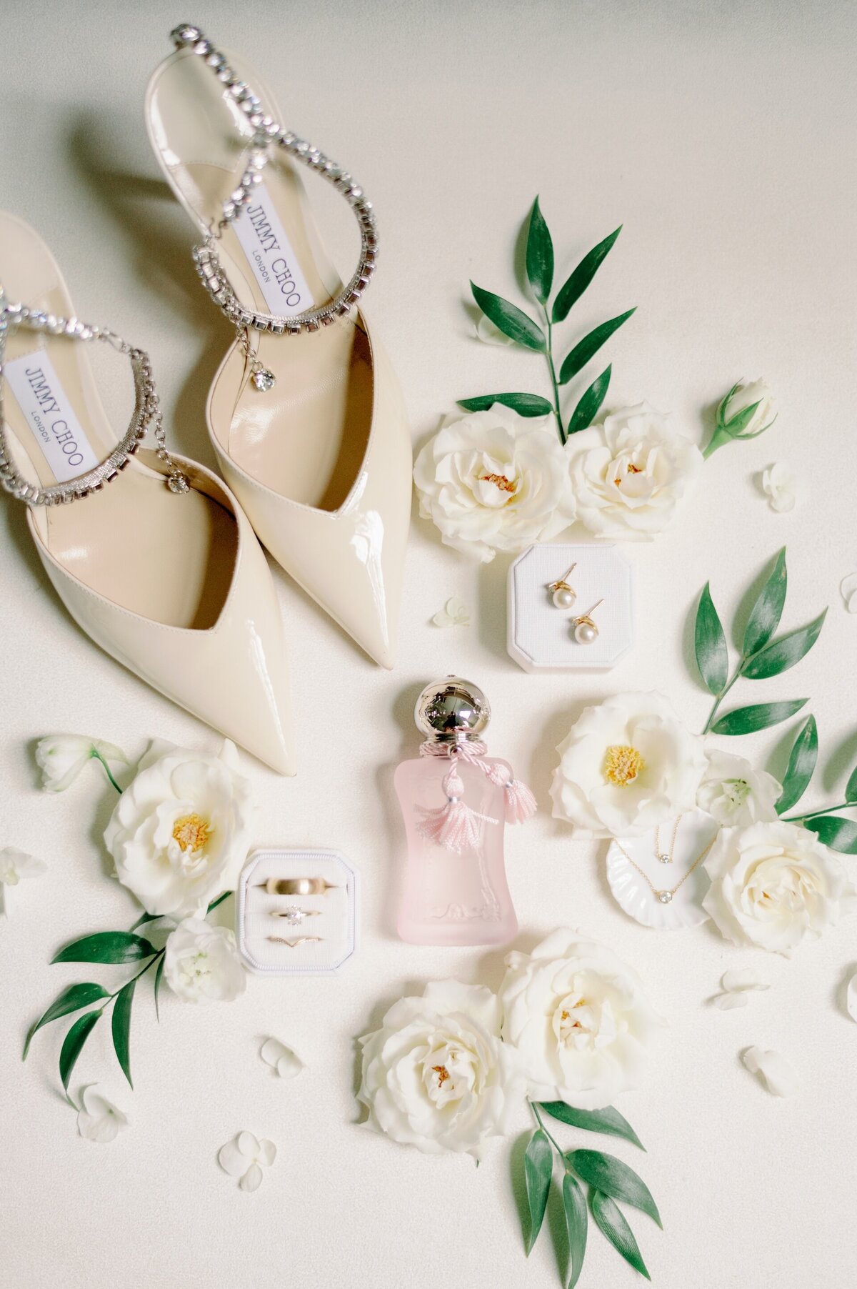 a flat lay of bridal items surrounded by flowers and greenery
