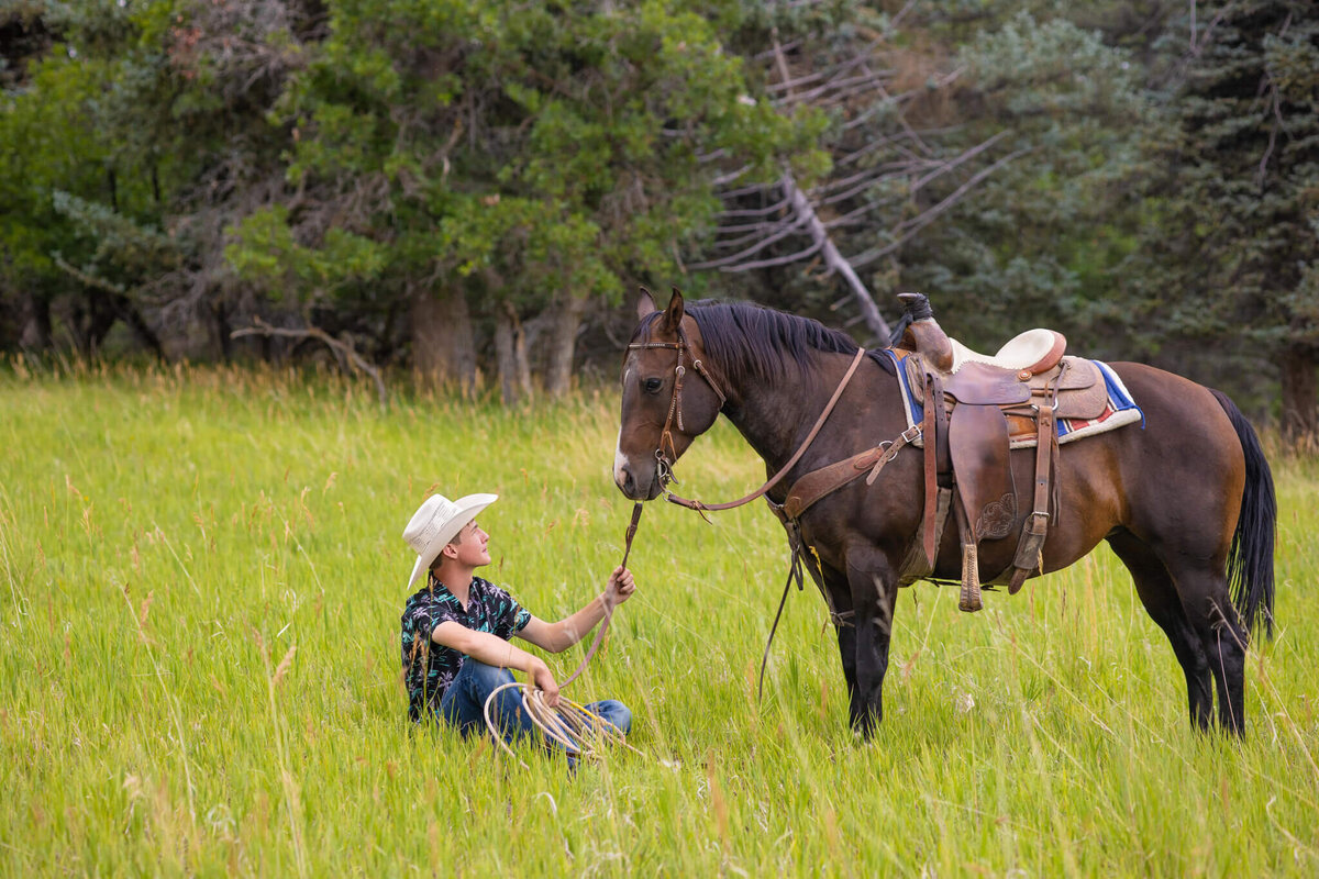teenage boy sitting in a grassy field with his horse holding the reins