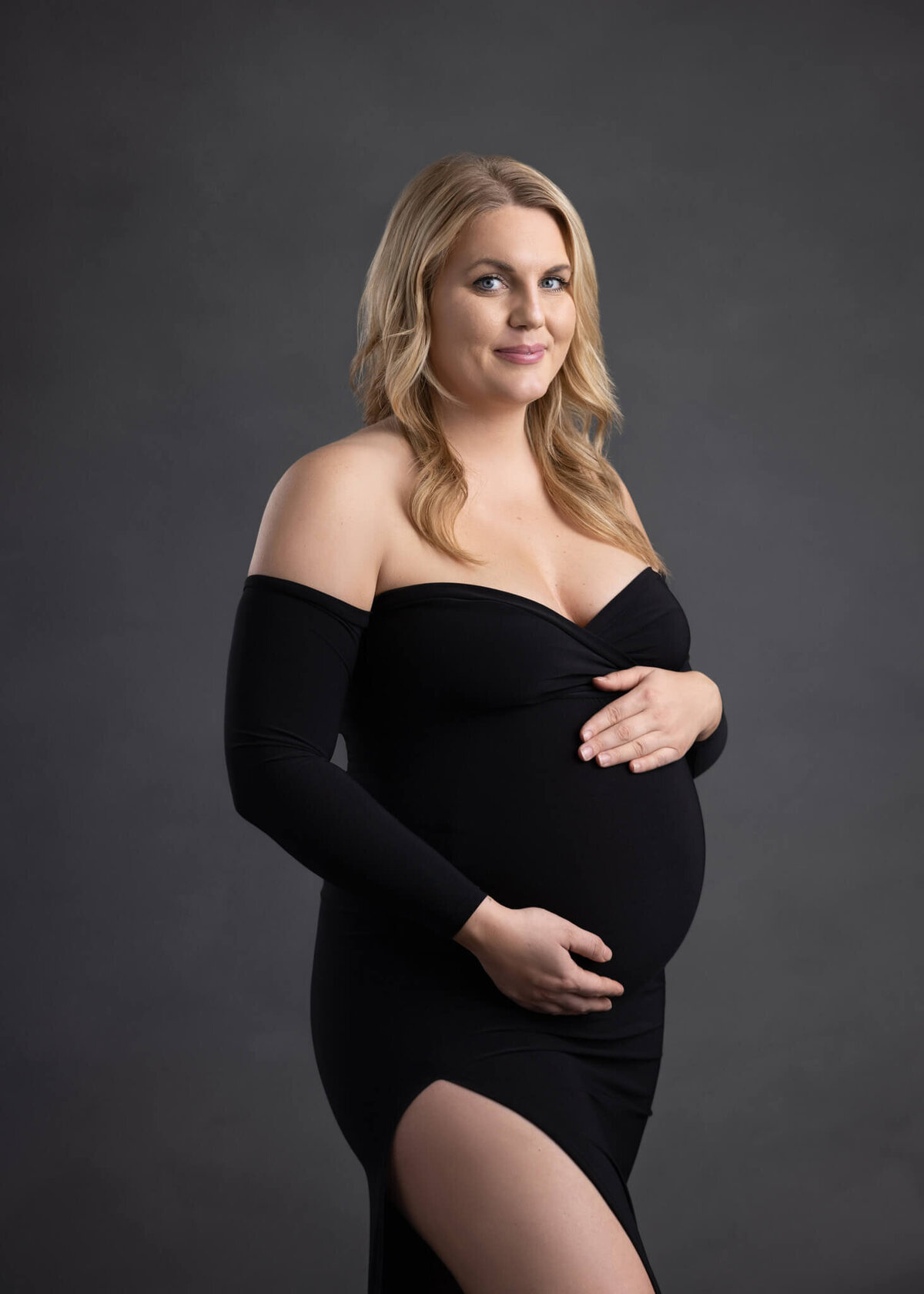 pregnant woman in a black dress holding her belly with both hands