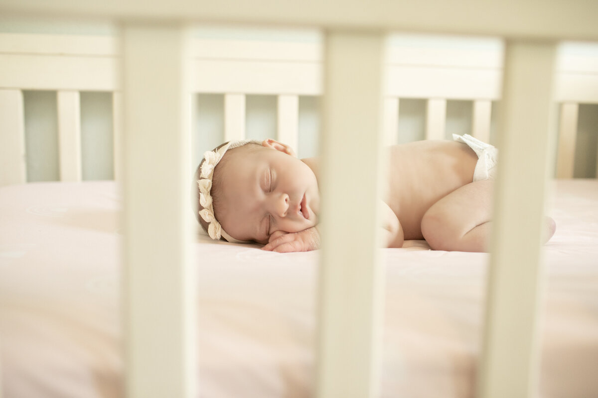 Newborn baby girl peacefully resting in a crib, surrounded by soft blankets, creating a cozy and serene scene