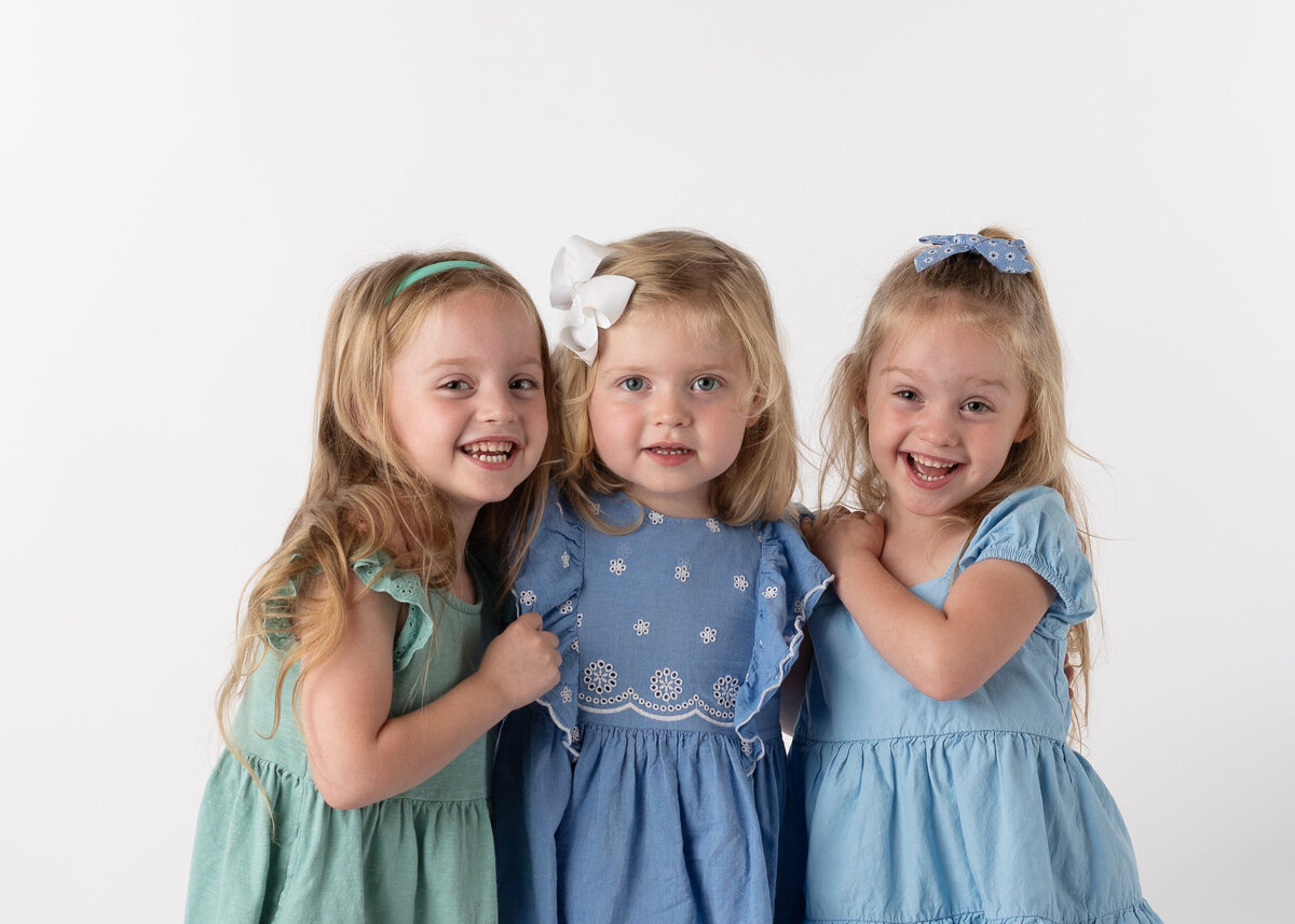 Three young sisters smiling proudly for their shcool picture.