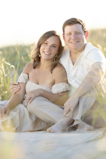 a couple sit in the dunes at golden hour during their engagement session in the Hamptons.