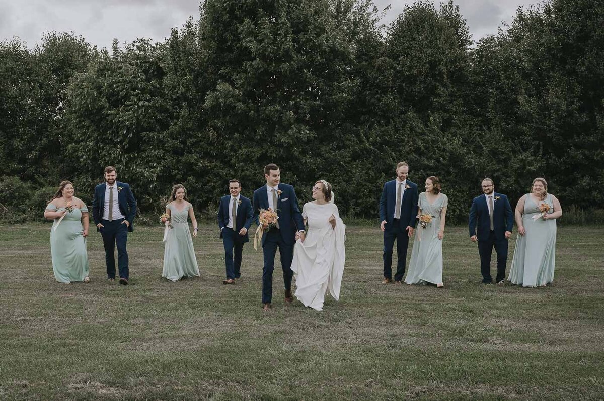 bridesmaids in green dresses and groomsmen in navy suits standing with bride and groom
