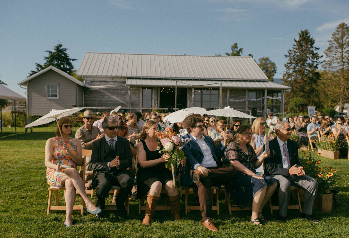 Guests wait in the sun for an outdoor ceremony to begin, surrounded by flowers and rustic charm—typical of laid-back Seattle wedding photography venues.