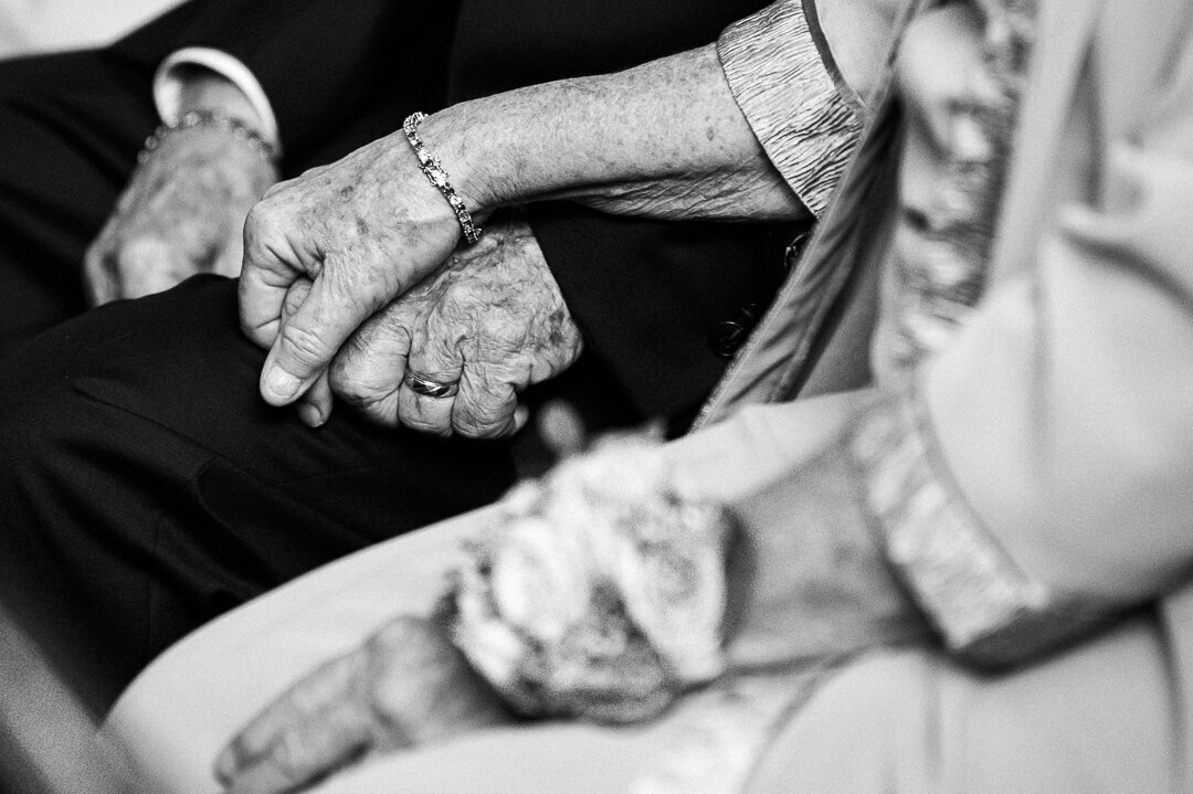 Black and white photo of grandparents holding hands tenderly during a New Jersey wedding ceremony.