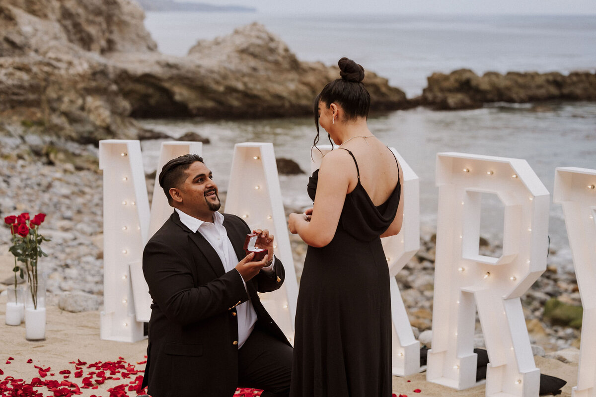 Marquee letters and red roses line the beach in palos verdes for this luxury surprise engagement.