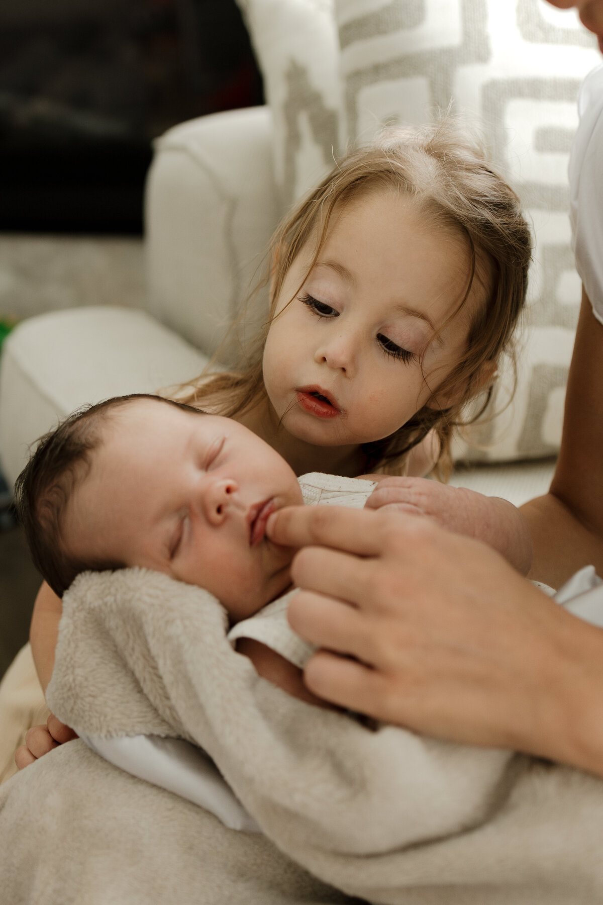 big sister looking over newborns shoulder while mom is touching newborns lip during lifestyle in home newborn session in longmont colorado with alexis adkins photo