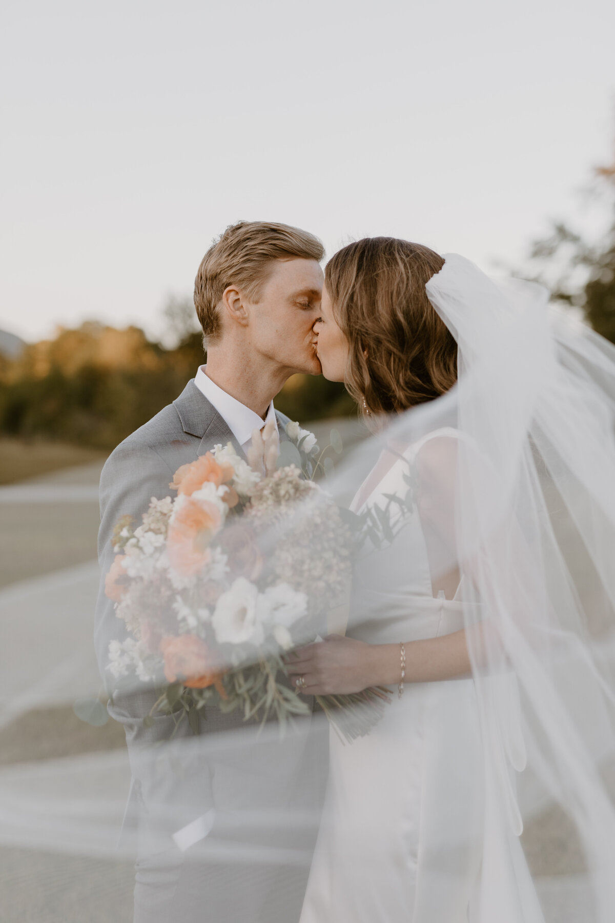 Newlyweds kissing at sunset surrounded by vineyard vines and warm light.