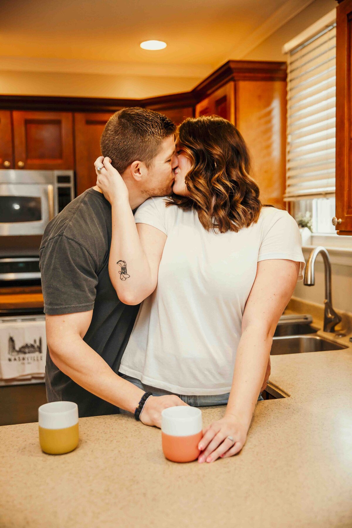 husband and wife kissing in kitchen with coffee mugs