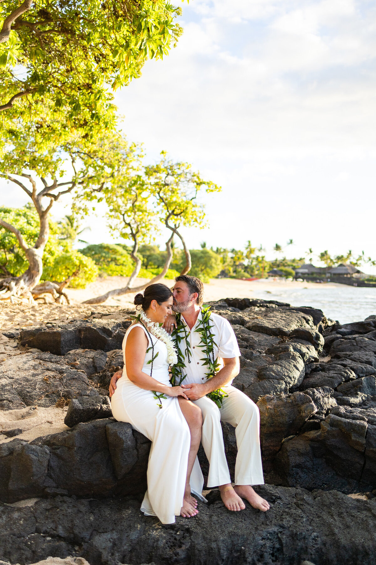 bride and groom on a hawaii beach kissing on lava rock