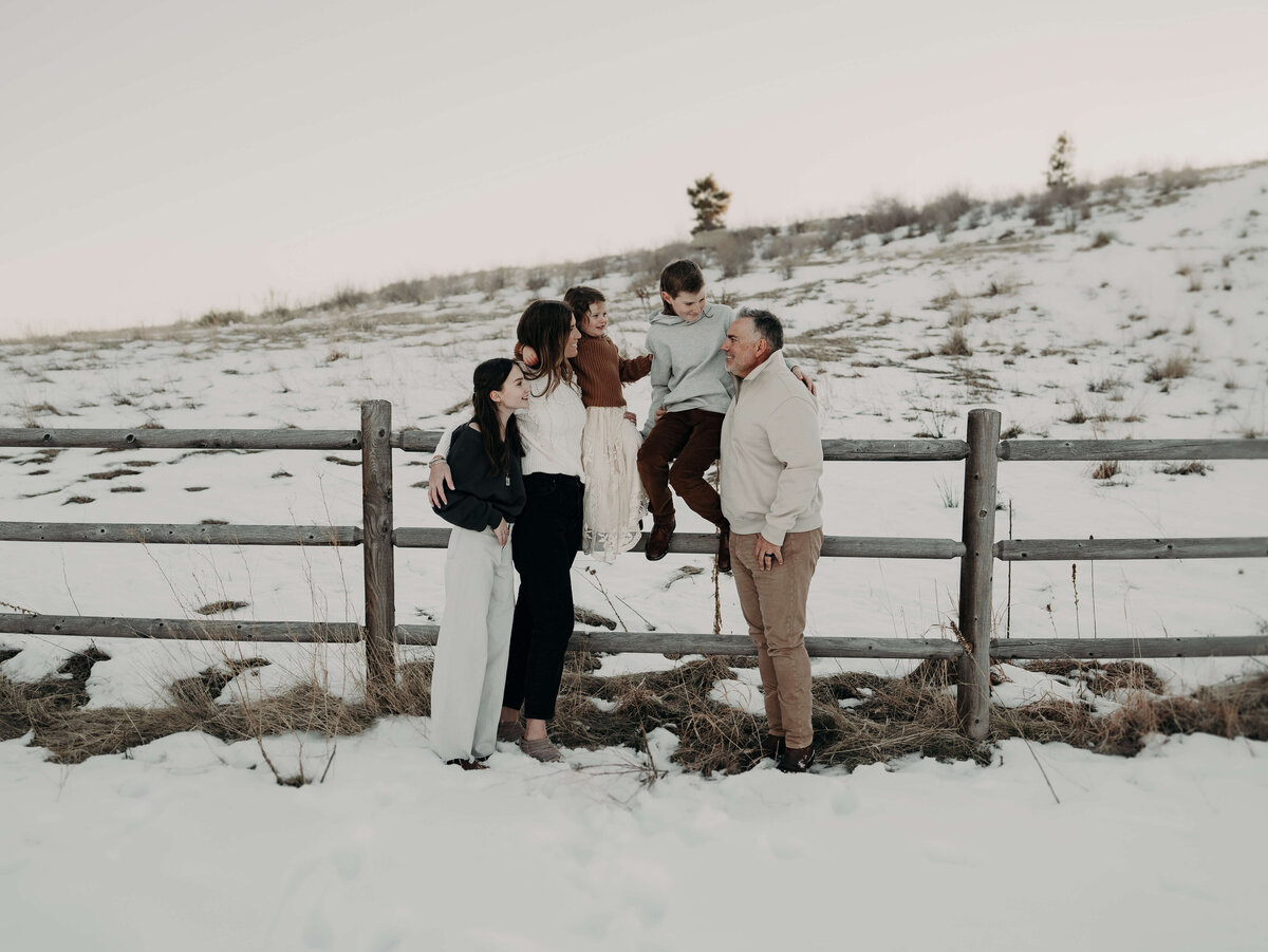 A family of five stylishly, dressed in winter cream, colored clothing poses organically along a fence on a Colorado farm just outside of Denver.