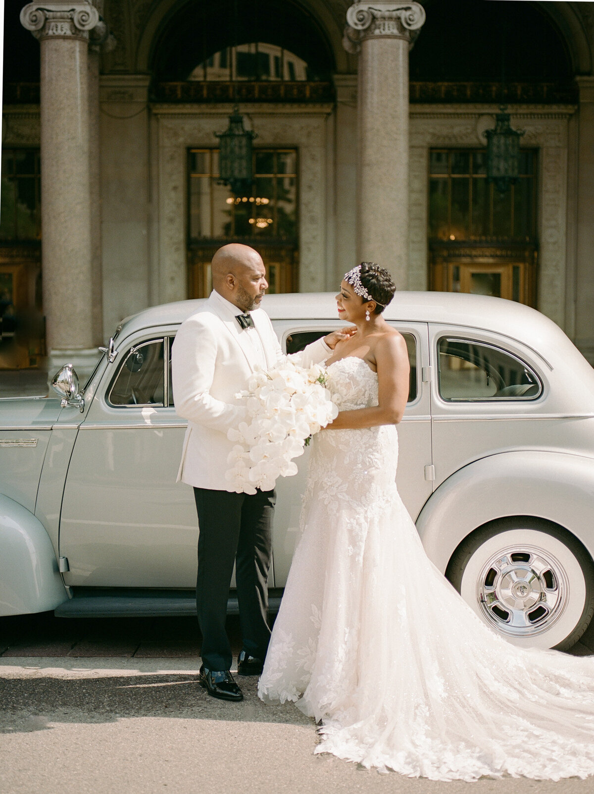 wedding couple smiles with vintage silver packard car and Detroit architecture