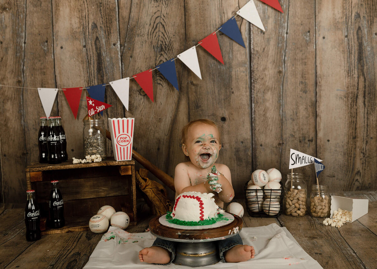 1 year old boy eating his baseball cake. Baseball themed decorations in the background.